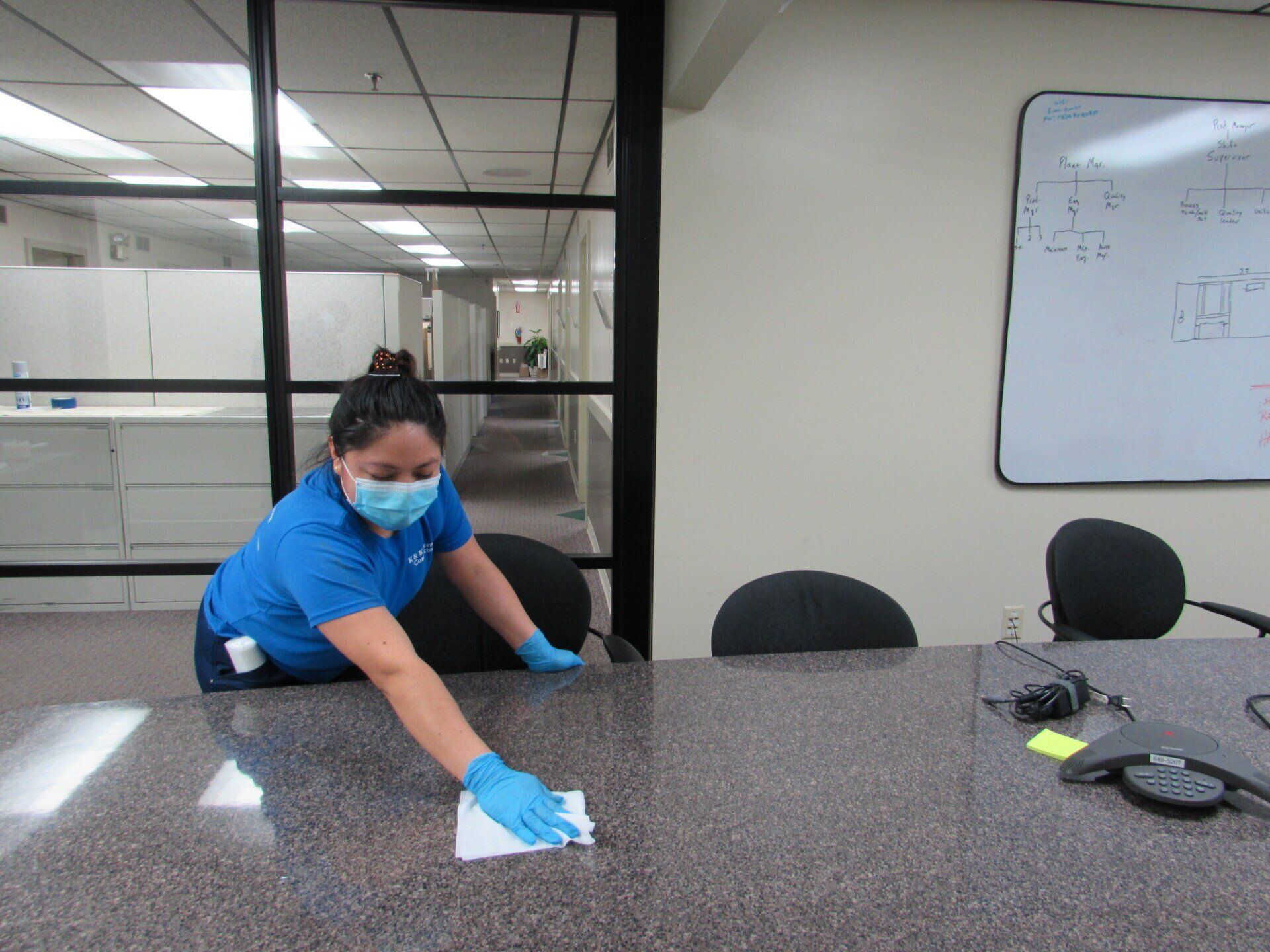 Office cleaner wiping down a conference table with disinfectant, wearing a mask and gloves.